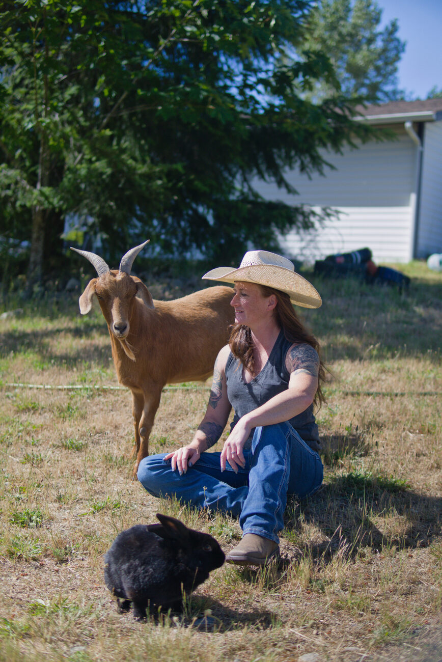 Founder kneeling beside a goat with a rabbit nearby